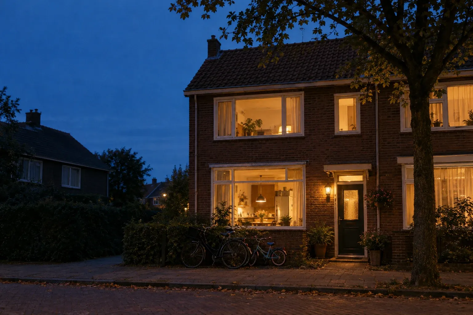 Een rijtjeshuis in de avond, met warm licht achter de ramen en fietsen voor de deur